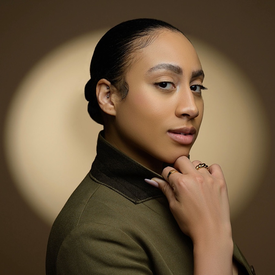 Portrait of Dev in an olive jacket, looking over one shoulder